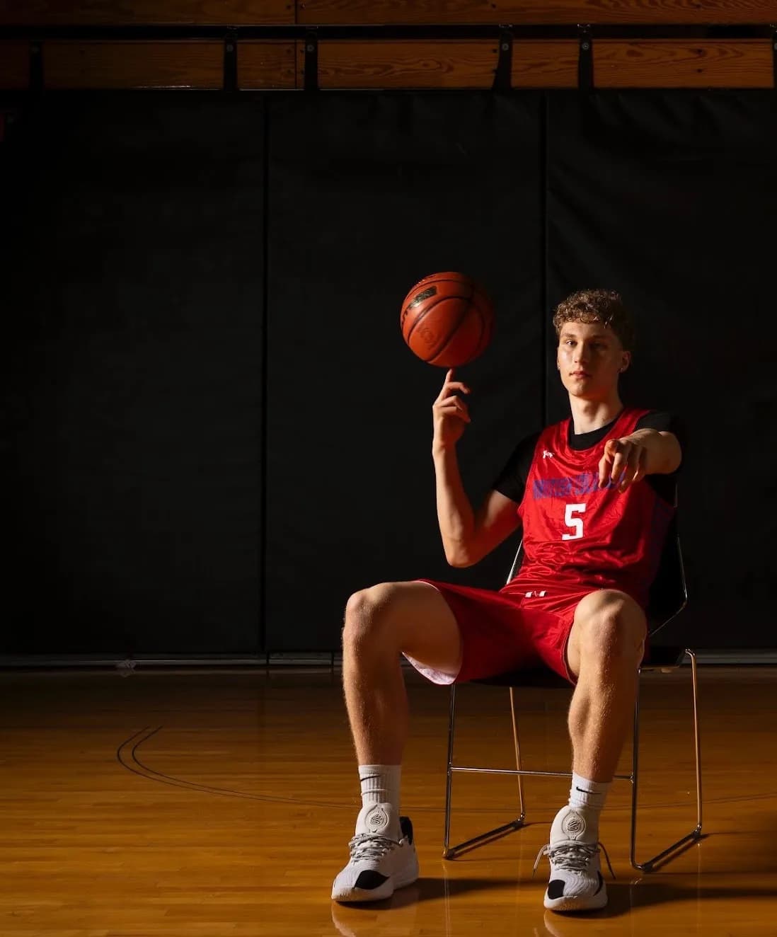 Nathan seated on a basketball court, balancing a basketball on one finger
